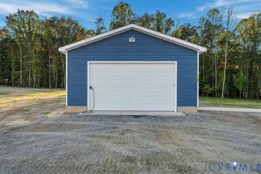 Detached garage featuring blue vinyl siding, a white overhead door, a concrete foundation, and an exterior wall-mounted light fixture Detached garage featuring blue vinyl siding, a white overhead door, a concrete foundation, and an exterior wall-mounted light fixture