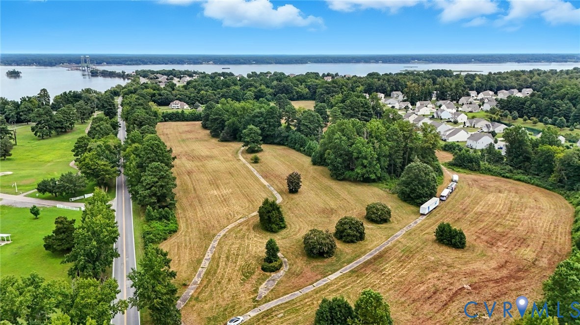 Expansive waterfront parcel featuring mature trees, cleared open land, paved pathways, and direct access to major roadways