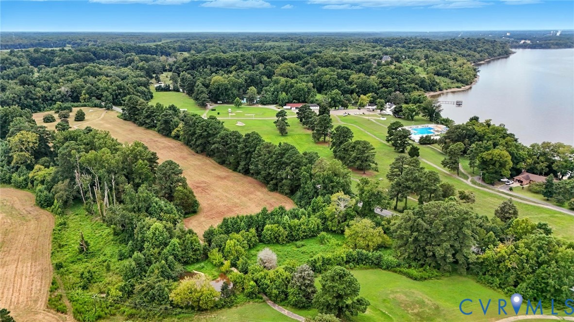 Aerial perspective featuring expansive acreage, mature tree clusters, open grass fields, and immediate proximity to a large body of water
