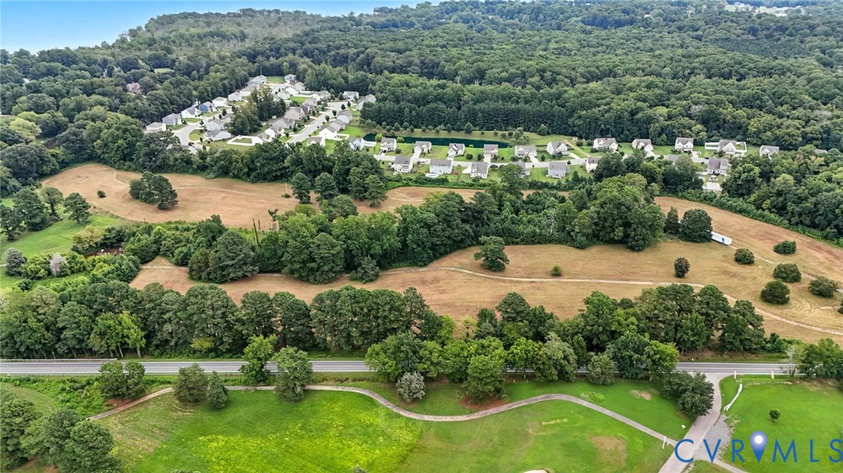 Aerial perspective of expansive acreage featuring vast open grassy fields, densely wooded areas, mature tree lines, and paved pathways