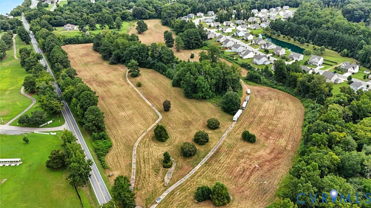 Expansive land parcel featuring rolling topography, mature tree clusters, and paved path access