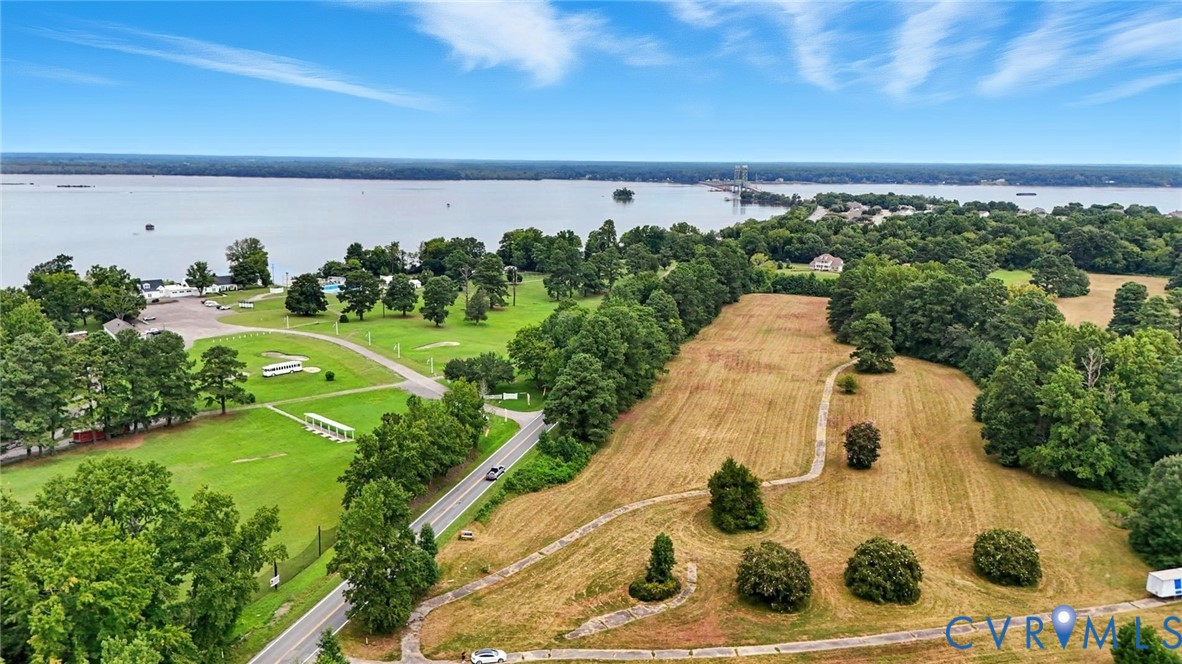 Aerial perspective of expansive acreage featuring mature trees, a meandering paved path, and direct proximity to a large body of water