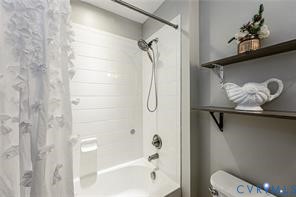 Bathtub with white surround, wall-mounted adjustable shower head, and two dark-finish wall-mounted open shelves