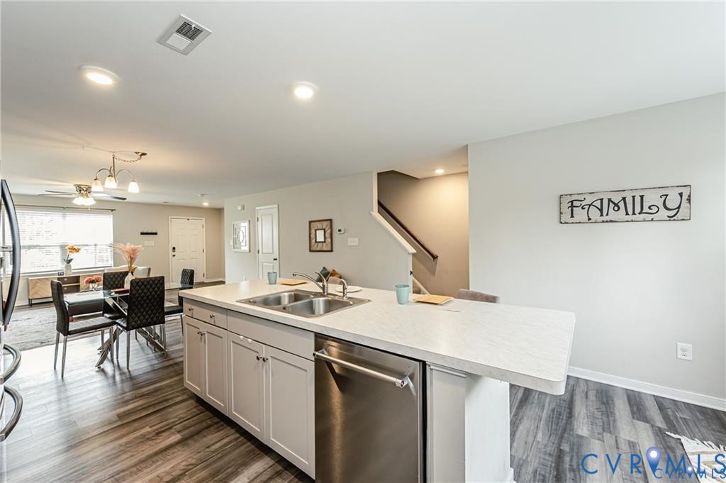 Kitchen island with a dual-basin stainless steel sink and stainless steel dishwasher, light-toned cabinetry, recessed lighting, and wood-finish flooring