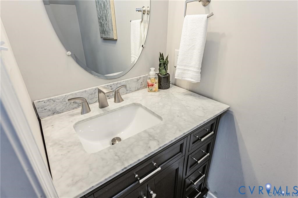 Dark-finish vanity featuring brushed nickel hardware, stone-top counter with an integrated basin, brushed nickel faucet, and oval wall-mounted mirror