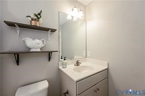 Bathroom featuring a vanity with a white countertop and integrated basin, chrome faucet, wall-mounted mirror, three-light fixture, and two dark-finished wall-mounted shelves