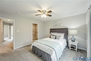 Neutral-toned room featuring a wood-panel headboard, recessed closet shelving, and a ceiling-mounted light fixture with a three-blade fan