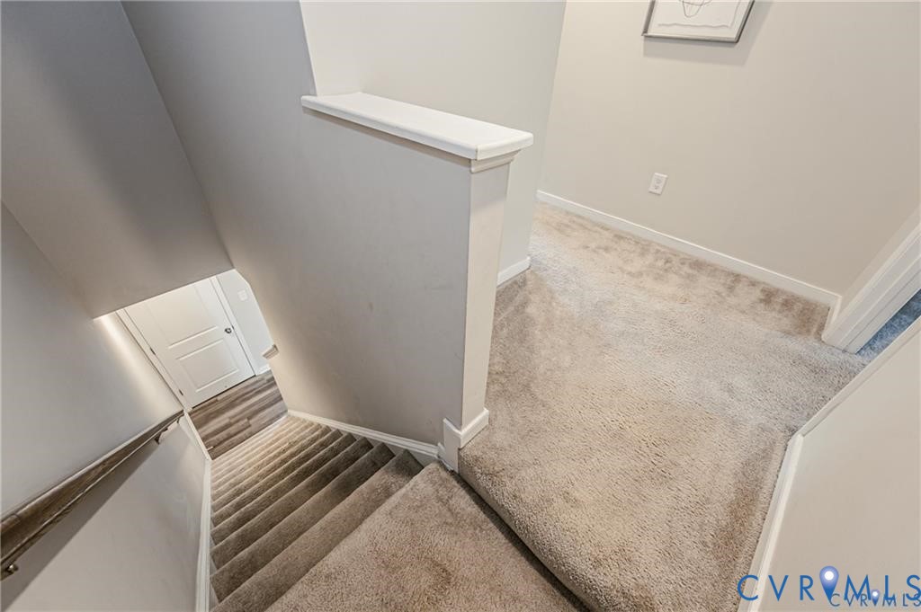 Staircase featuring neutral carpeting, a painted half-wall with a cap, and a minimalist metal handrail