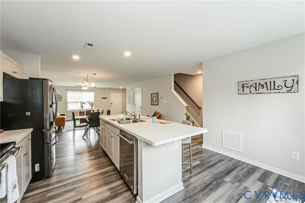 Kitchen featuring a central island with a dual-basin stainless steel sink, white cabinetry, integrated stainless steel dishwasher, recessed lighting, and wood-finish flooring