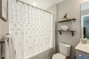 Bathroom featuring a built-in shower-tub combination, wall-mounted open shelving, a standard toilet, and a vanity with a countertop basin
