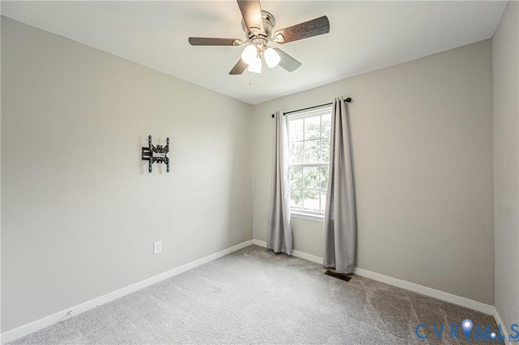 Neutral-toned room featuring wall-to-wall carpeting, a multi-light ceiling fan, a window with an integrated curtain rod, and a wall-mounted bracket