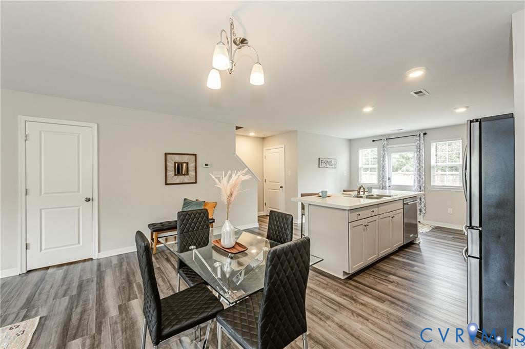 Open-concept kitchen and dining area featuring wood-finish flooring, a central island with integrated sink, recessed lighting, and a multi-light chandelier