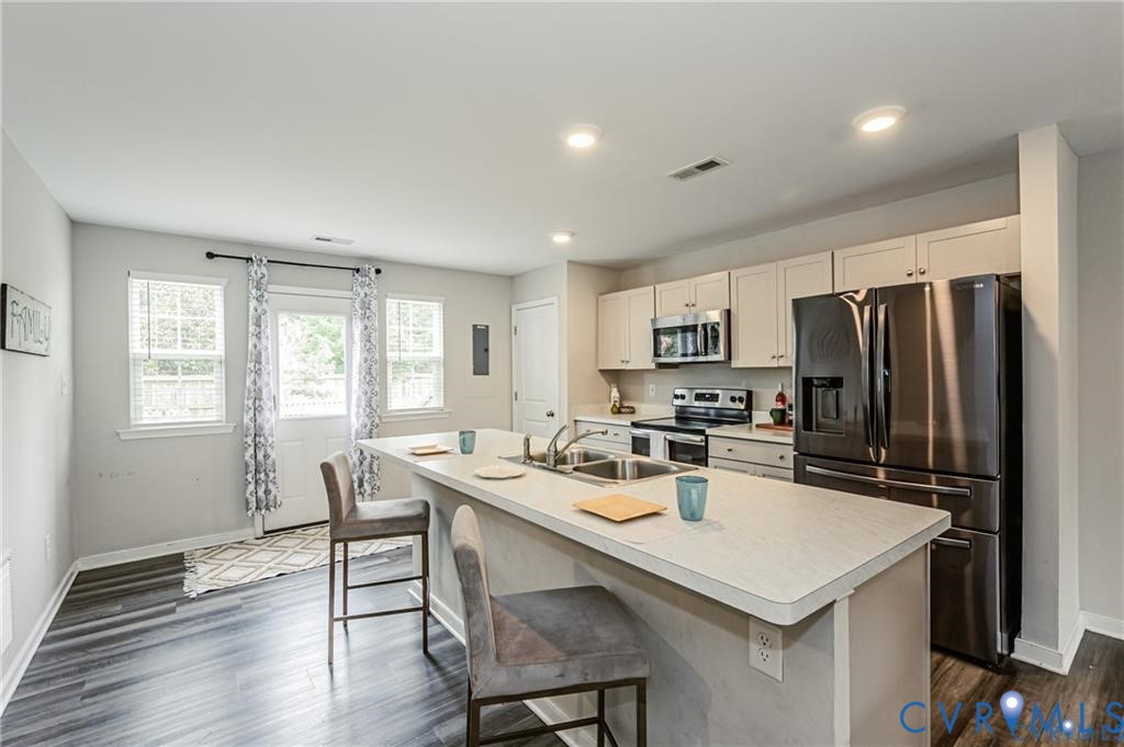 Kitchen featuring an island with a stainless steel dual-basin sink, light-toned cabinetry, stainless steel appliances, and wood-finish flooring