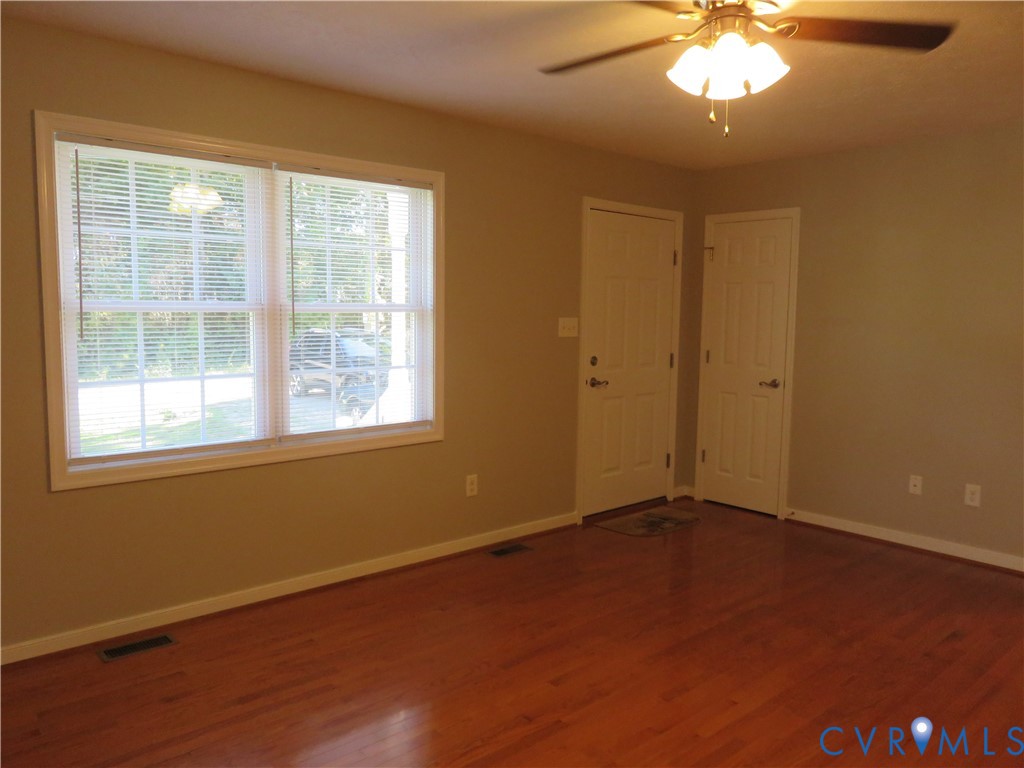 Room featuring wood-finish flooring, a large multi-pane window, two white paneled doors, and an attached ceiling fan with light fixture Room featuring wood-finish flooring, a large multi-pane window, two white paneled doors, and an attached ceiling fan with light fixture