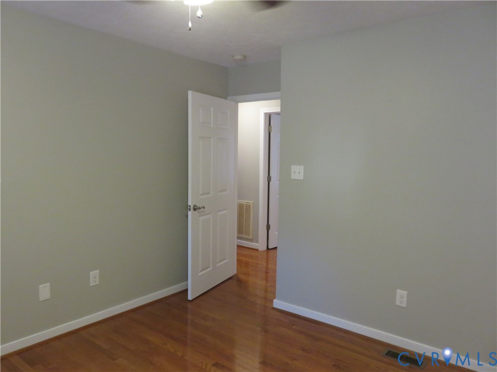 Interior space featuring neutral-toned walls, wood-finish flooring, a white six-panel door, and a ceiling-mounted light fixture