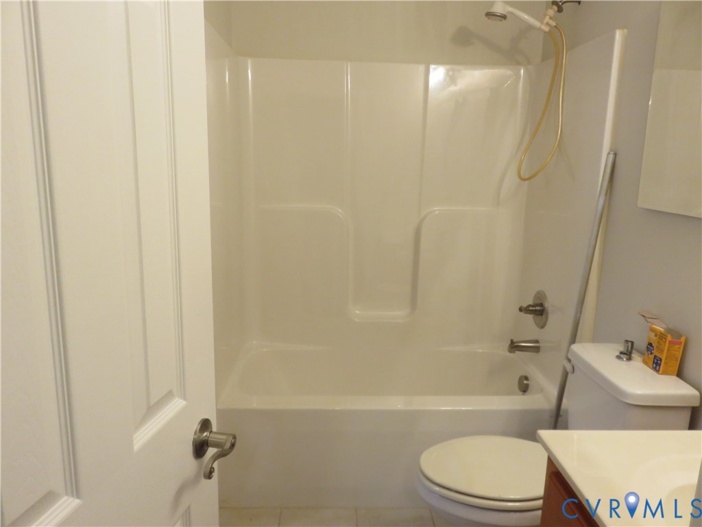 Bathroom featuring a white molded tub-and-shower surround with a handheld showerhead, a dual-handle faucet, a white porcelain toilet, and a vanity with a white countertop