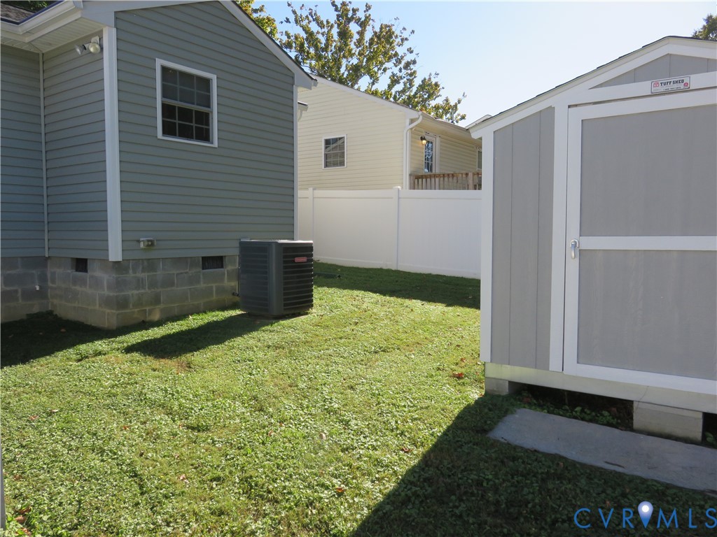 Exterior space featuring a vinyl-sided home with a concrete block foundation, a detached storage building, and a vinyl privacy fence