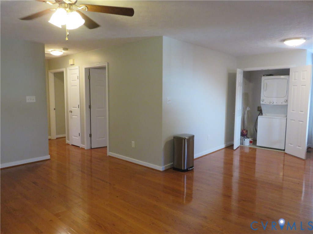 Interior featuring wood-finish flooring, ceiling fan with integrated lighting, multiple paneled doors, and a laundry closet with stacked laundry appliances Interior featuring wood-finish flooring, ceiling fan with integrated lighting, multiple paneled doors, and a laundry closet with stacked laundry appliances