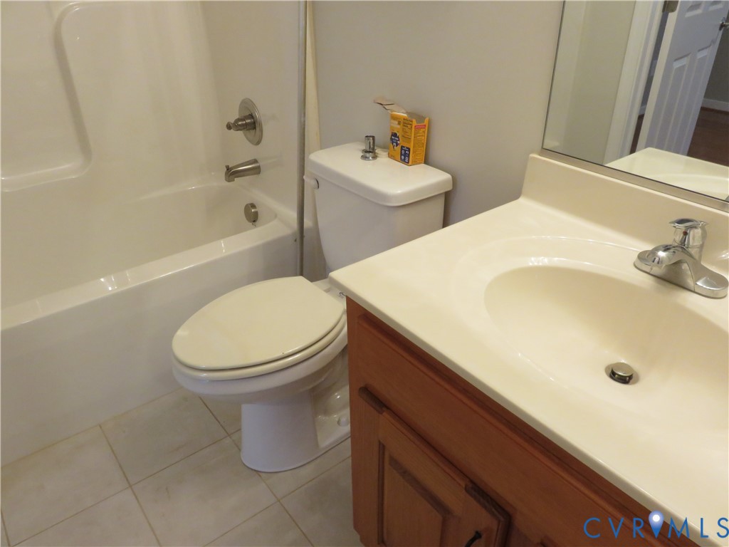 Bathroom featuring a wood-finish vanity with a molded countertop, integrated sink, chrome-finish faucet, and a tub-shower combination with tile flooring