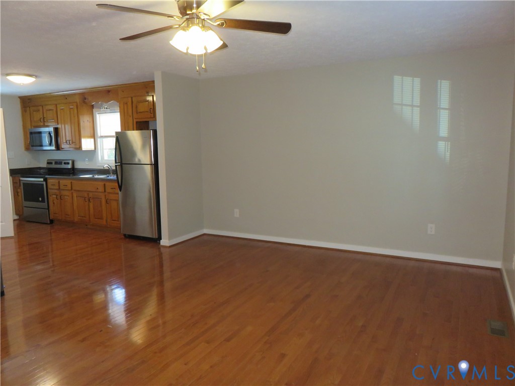 Kitchen featuring wood cabinetry, stainless steel appliances, wood-finish flooring, and a ceiling-mounted light fixture Kitchen featuring wood cabinetry, stainless steel appliances, wood-finish flooring, and a ceiling-mounted light fixture