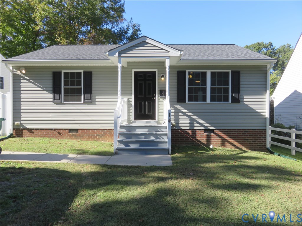 Single-story exterior featuring light-toned vinyl siding, brick foundation, dark-toned shutters, and a covered front stoop with white railings