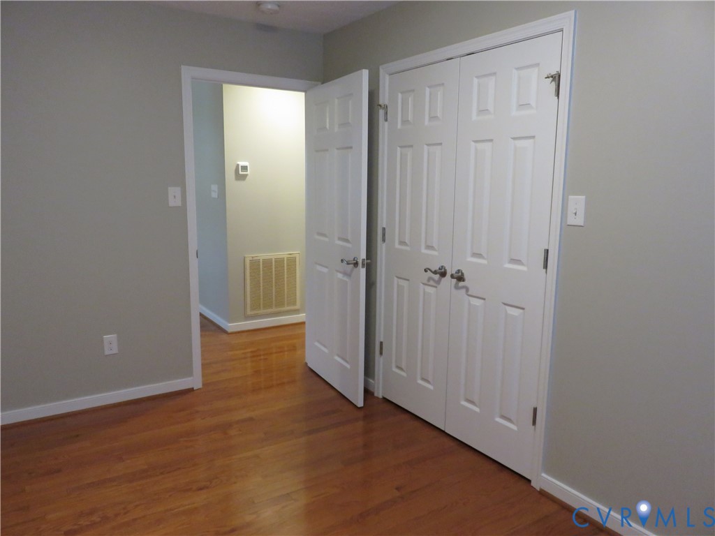 Wood-finish flooring, white six-panel interior doors, and double-door closet with satin-finish hardware