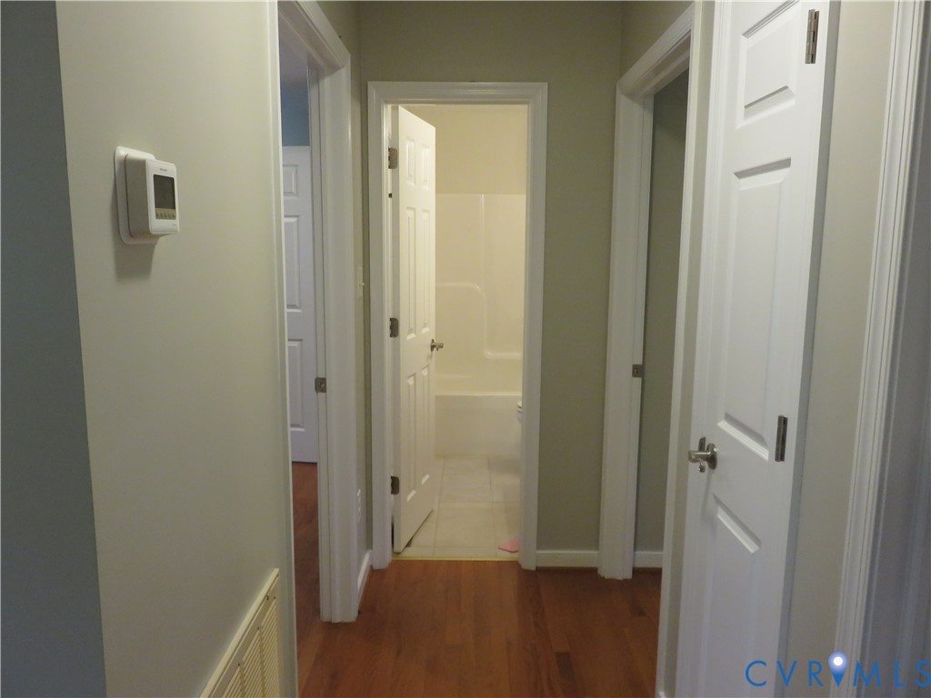 Interior hallway featuring wood-finish flooring, white paneled doors, neutral wall paint, and a programmable wall-mounted thermostat