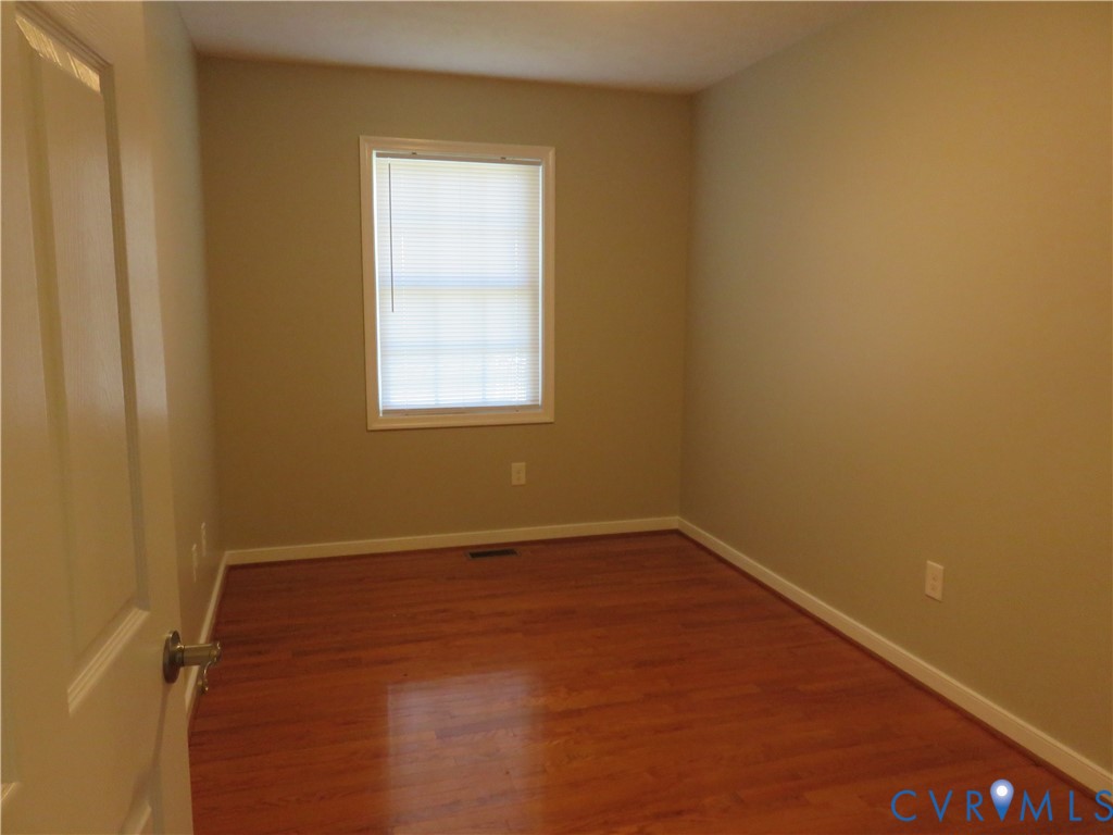 Room with wood-finish flooring, neutral-toned walls, and a single window featuring integrated blinds
