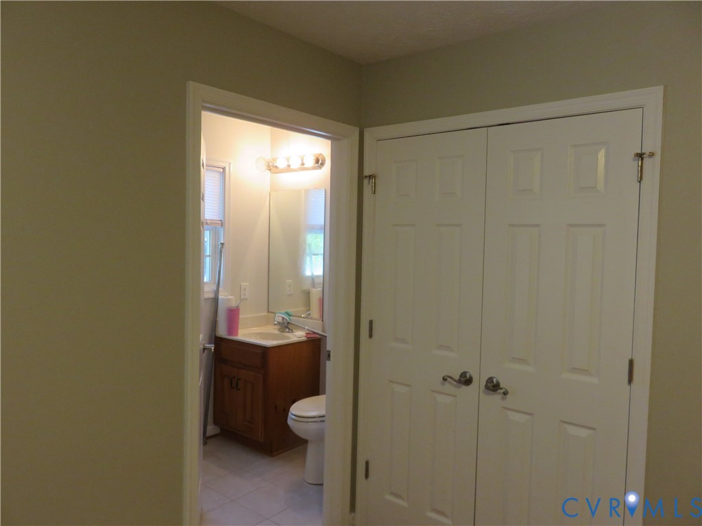 Six-panel white closet doors and interior bathroom featuring a wood-finish vanity, wall-mounted mirror, and multi-bulb light fixture