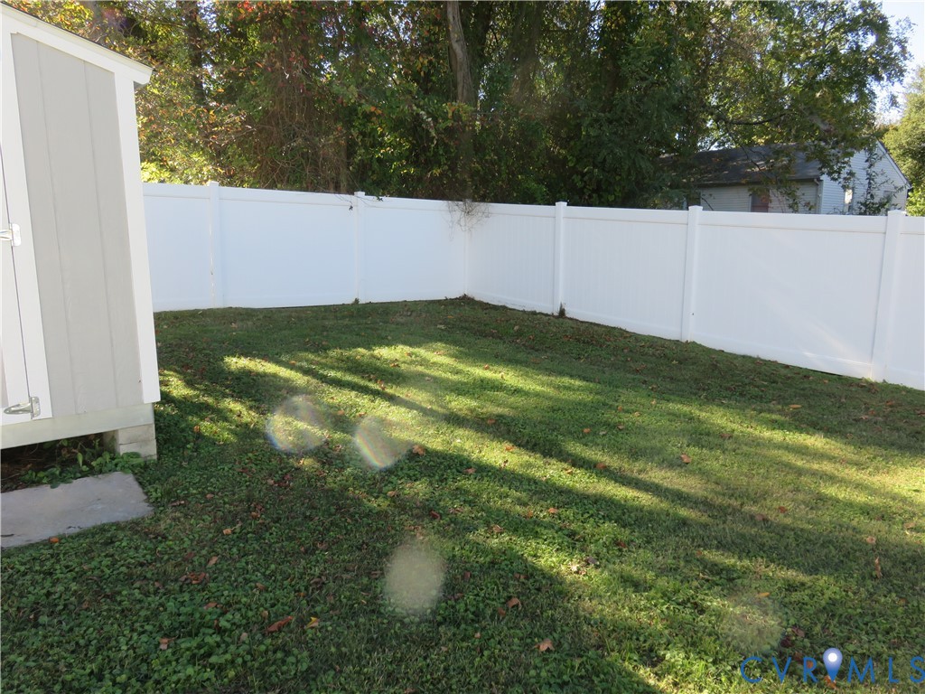 Backyard featuring a white vinyl privacy fence and a detached storage structure on a concrete foundation