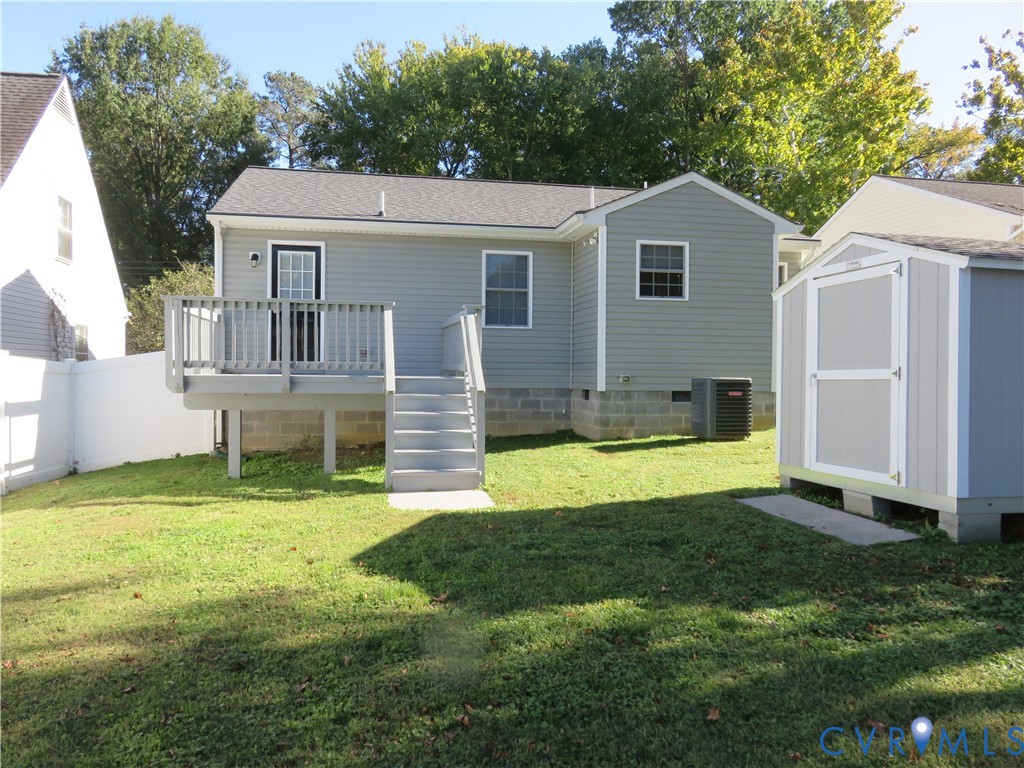 Rear exterior featuring gray vinyl siding, an elevated wood deck with stairs, a detached storage shed, and a white privacy fence