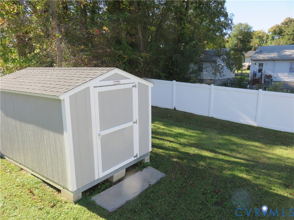 Detached storage shed featuring grey composite siding, a shingled roof, and a single-door entry, situated within a fenced rear yard