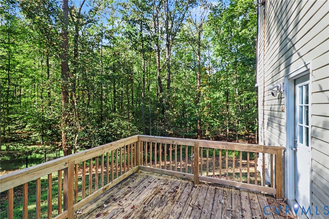 Elevated wood deck with a simple railing, light-colored vinyl siding, and exterior entry door, set against a backdrop of mature trees