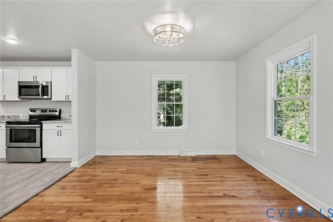 Open-concept space featuring wood-finish flooring, white cabinetry, stainless steel appliances, dual-pane windows, and a decorative flush-mount ceiling fixture