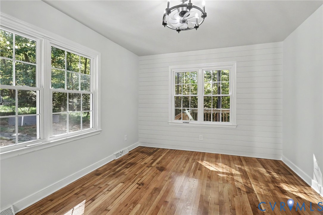 Room featuring wood-finish flooring, shiplap wall detailing, multi-pane windows, and a decorative ceiling fixture