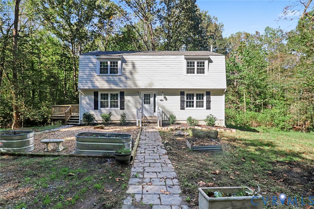 Two-story exterior featuring light-toned horizontal siding, a Gambrel roofline, stone-style paver walkway, and an attached side deck Two-story exterior featuring light-toned horizontal siding, a Gambrel roofline, stone-style paver walkway, and an attached side deck