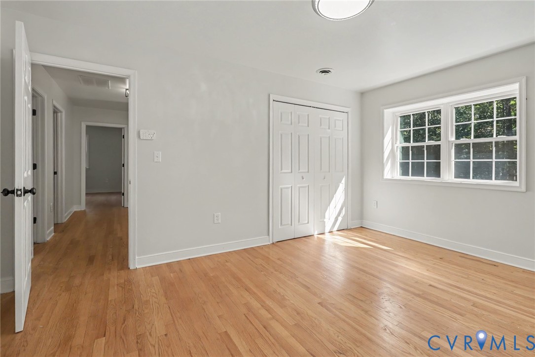 Room featuring wood-finish flooring, crisp neutral wall paint, white six-panel closet doors, and multi-pane windows with white trim
