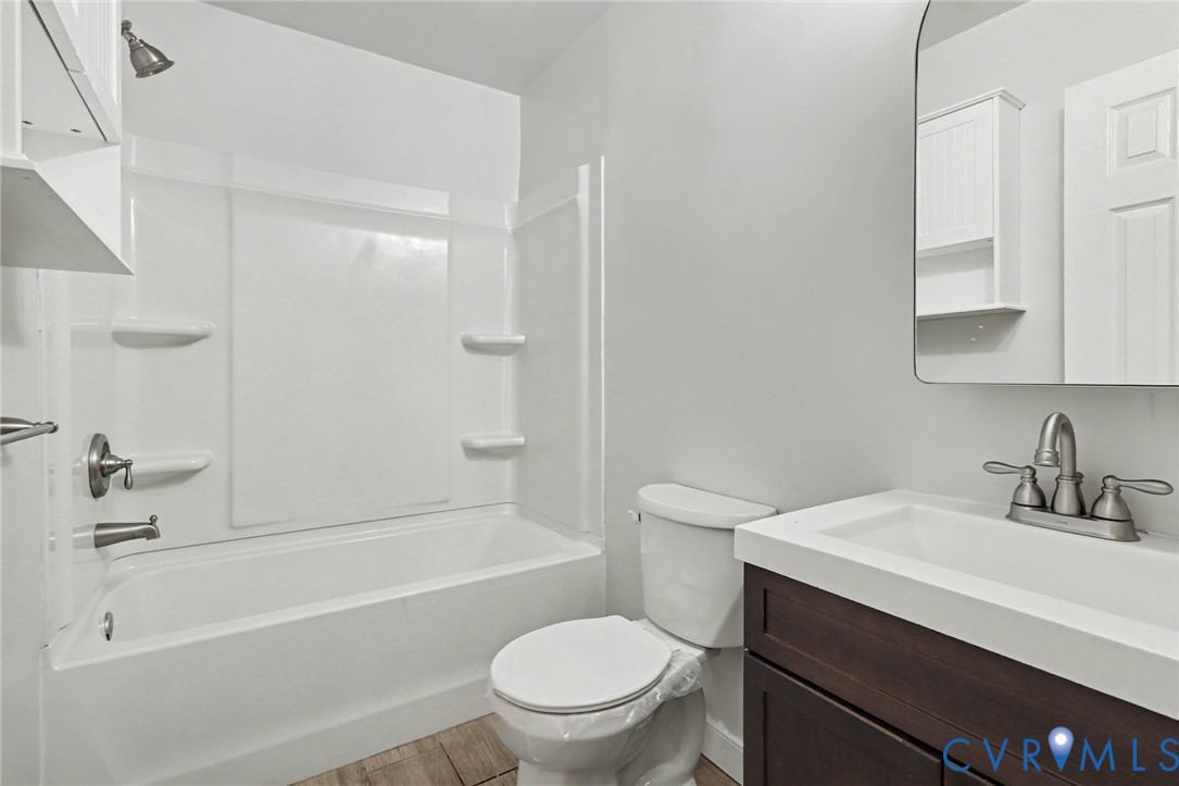 Bathroom featuring a dark wood-finish vanity with a rectangular integrated sink, brushed nickel faucet hardware, tub-shower combination with built-in shelving, and an arched wall mirror