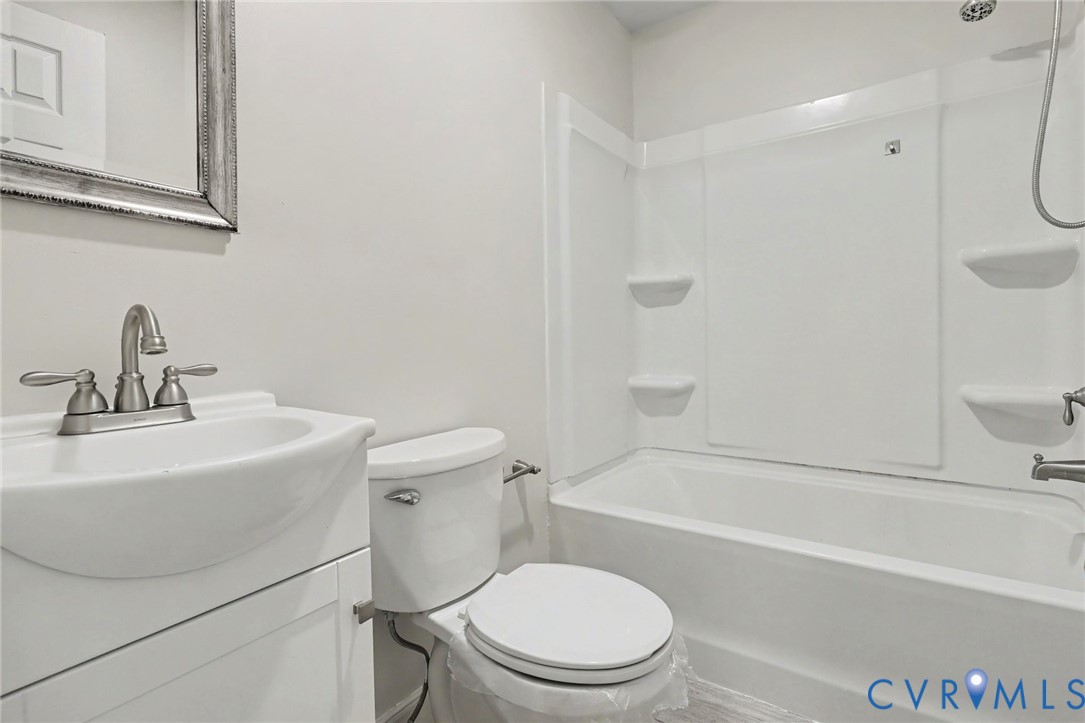 Bathroom featuring a white vanity cabinet with a integrated sink, dual-handle faucet, elongated toilet, and a combined tub and shower unit with built-in shelving