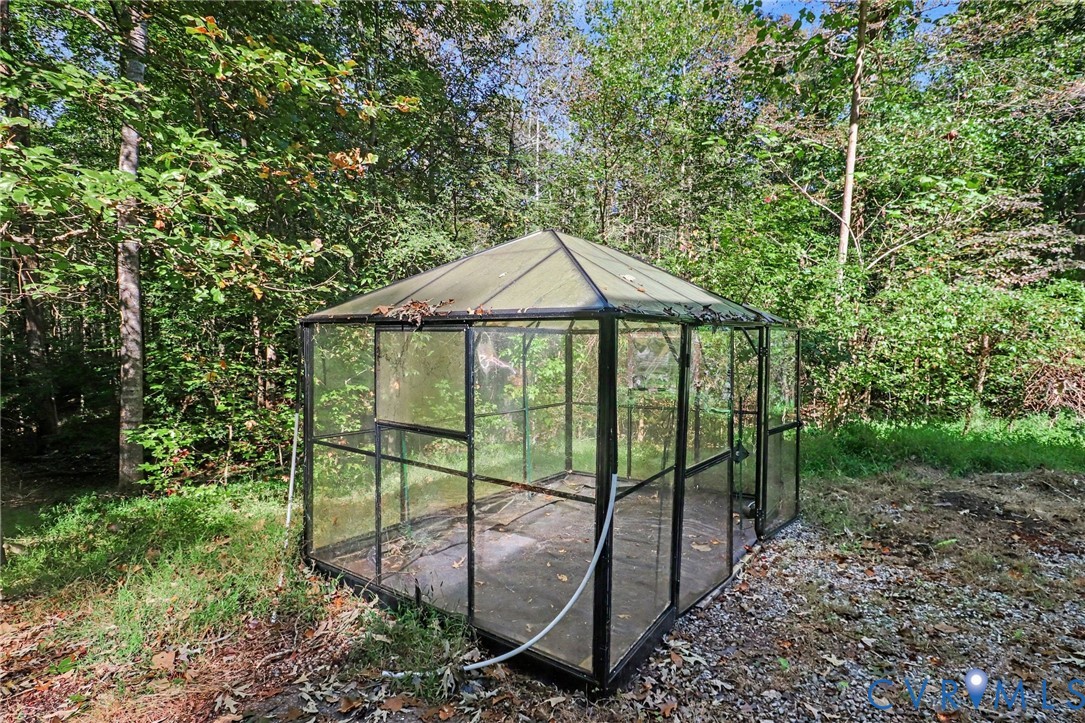 Free-standing greenhouse featuring black metal framing, glass paneling, and a pitched roof