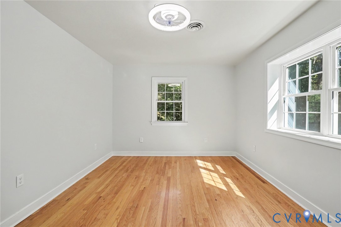 Neutral interior space featuring wood-finish flooring, multi-pane windows, and a circular LED flush-mount ceiling light