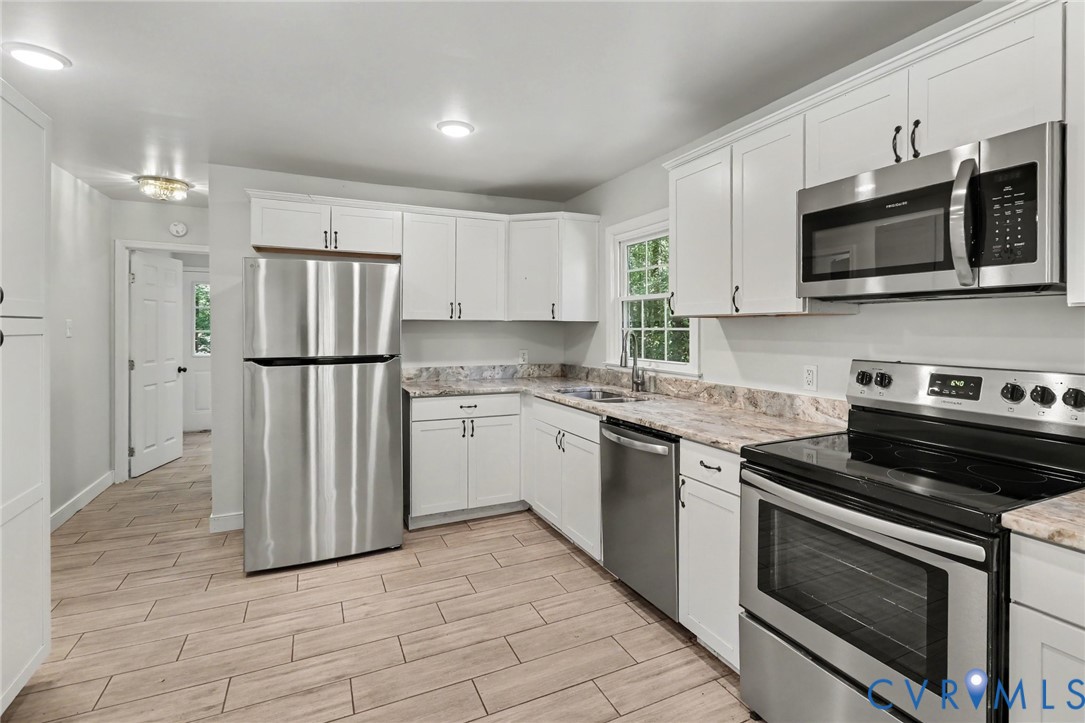 Kitchen featuring white shaker-style cabinetry, stainless steel appliances, neutral stone-patterned countertops, and wood-finish tile flooring