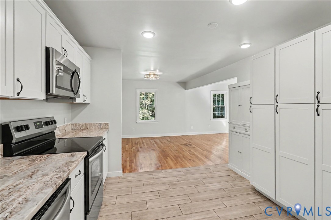 Kitchen featuring white shaker-style cabinetry, stone-pattern laminate countertops, stainless steel appliances, tile flooring, and wood-finish flooring