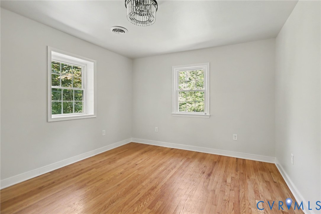 Room featuring wood-finish flooring, two double-hung windows with muntin grids, and a central tiered crystal light fixture