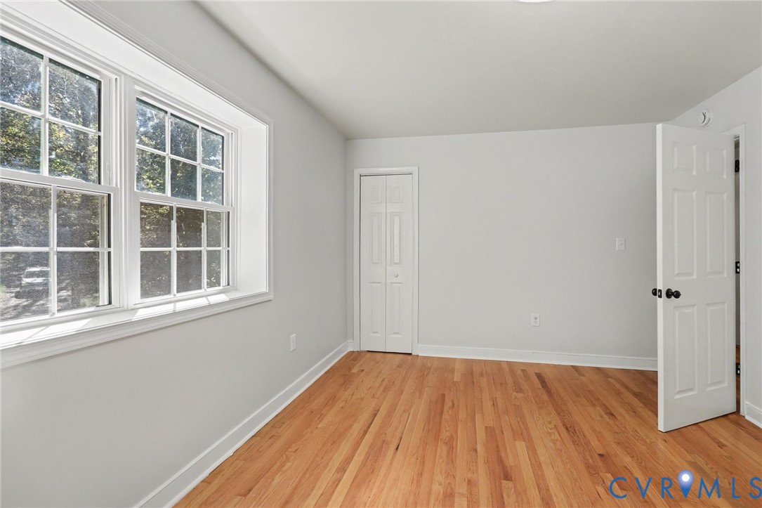 Room featuring wood-finish flooring, multi-pane window, bi-fold closet doors, and a six-panel door with matte black hardware