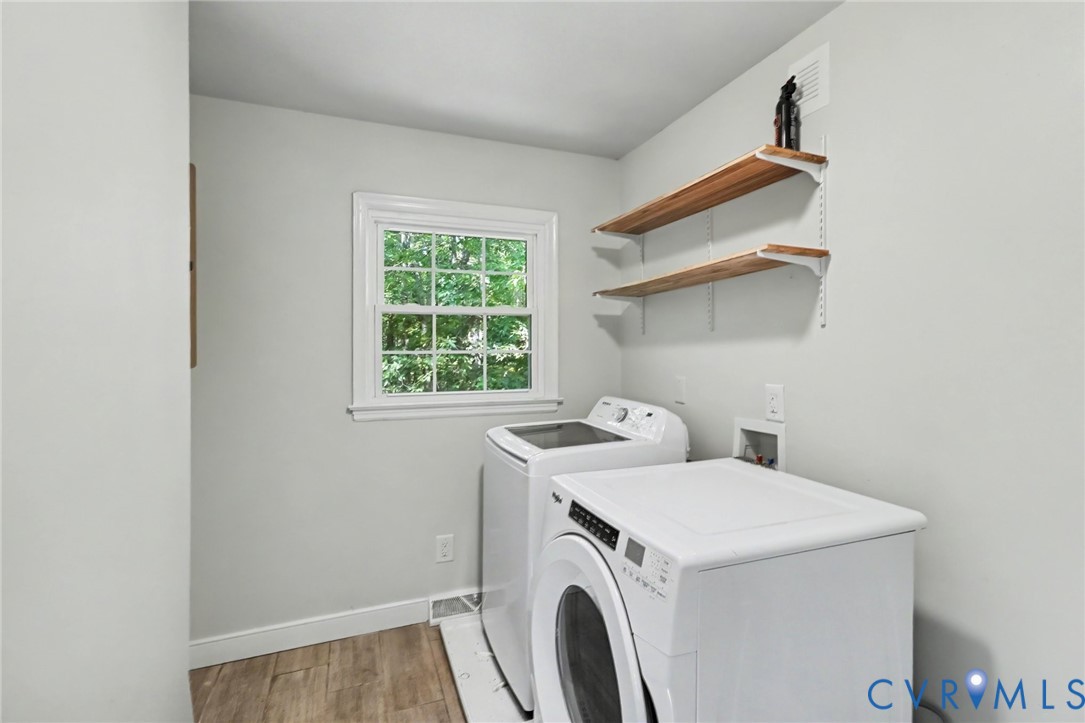 Laundry room featuring wood-finish flooring, double-hung window, and wall-mounted wood shelving