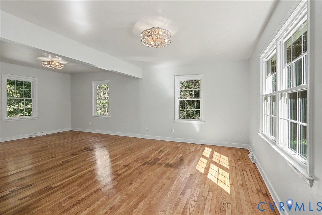 Room featuring wood-finish flooring, white walls, multiple windows with grid detailing, and two circular metal flush-mount light fixtures