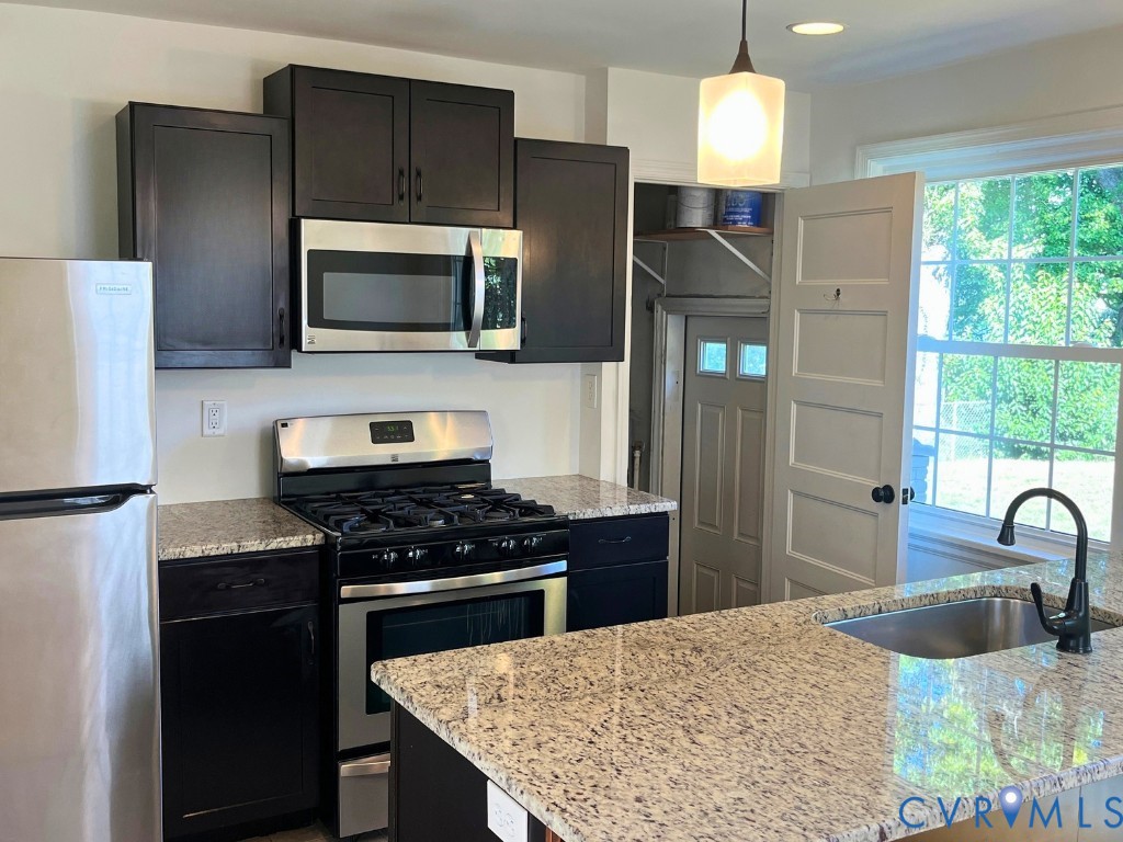 Kitchen featuring espresso cabinetry, stone-surface countertops, stainless steel gas range, microwave, and an undermount sink with a matte black faucet Kitchen featuring espresso cabinetry, stone-surface countertops, stainless steel gas range, microwave, and an undermount sink with a matte black faucet