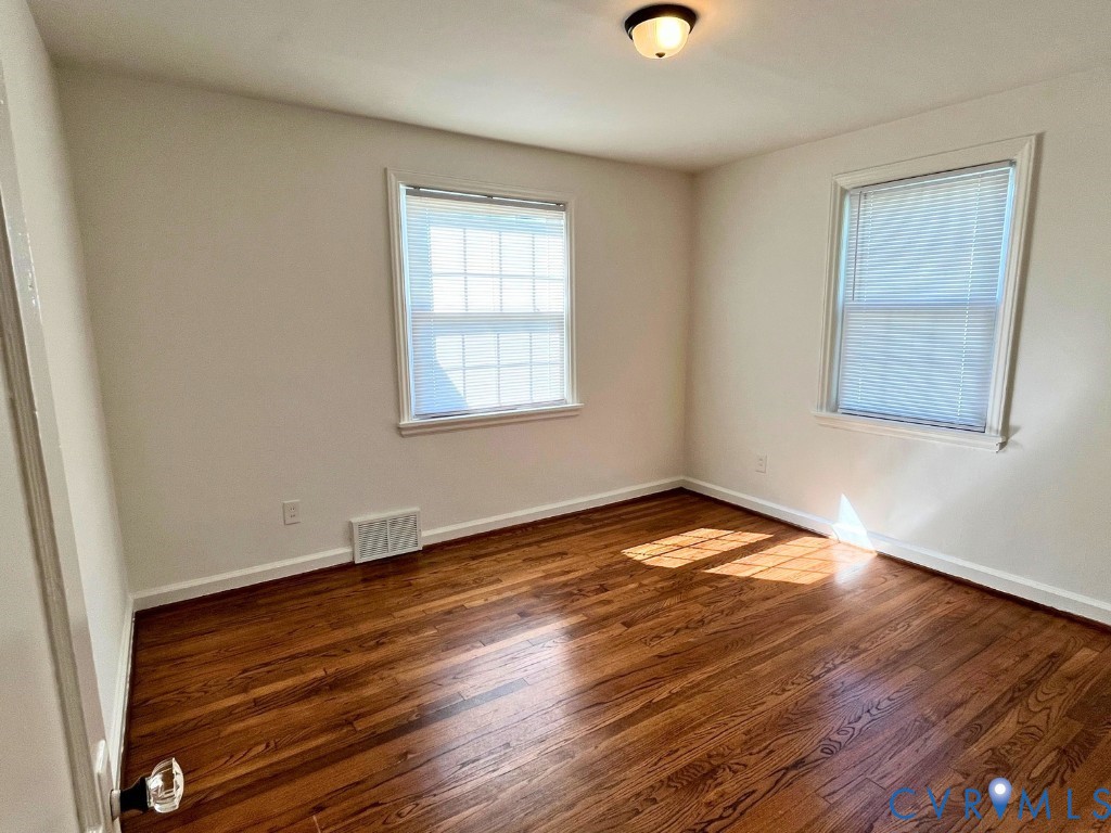 Room featuring wood-finish flooring, neutral wall paint, two windows with grid patterns, and a ceiling-mounted light fixture Room featuring wood-finish flooring, neutral wall paint, two windows with grid patterns, and a ceiling-mounted light fixture