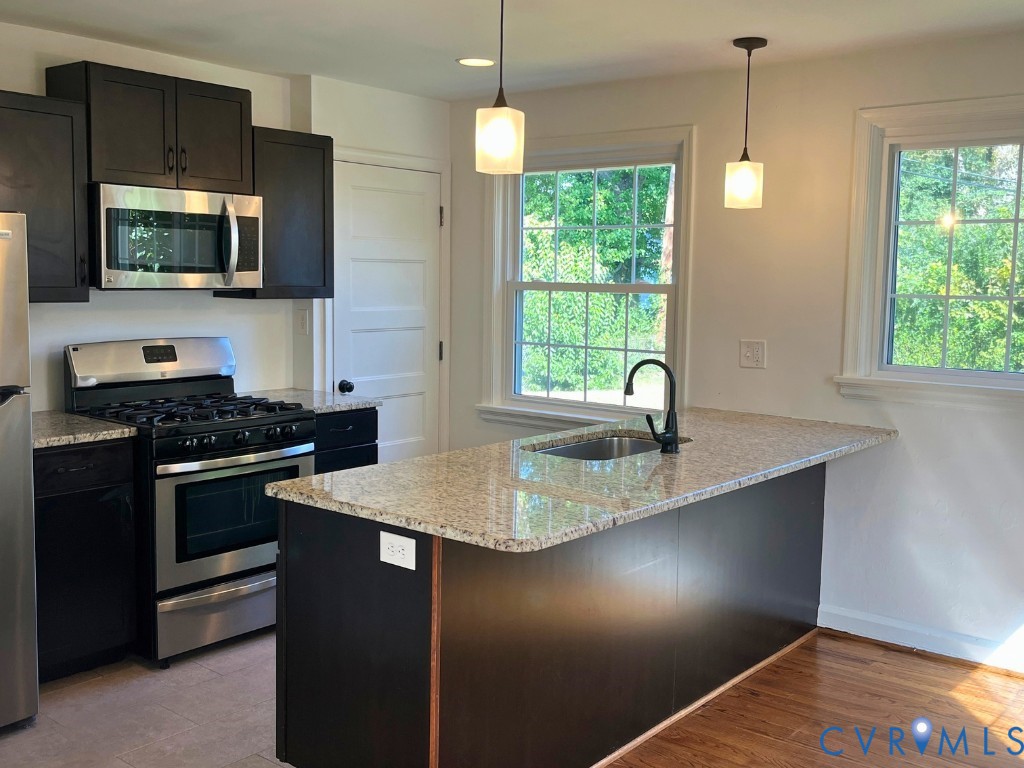 Kitchen featuring dark cabinetry, stone countertops, stainless steel gas range, integrated island with sink, and pendant lighting Kitchen featuring dark cabinetry, stone countertops, stainless steel gas range, integrated island with sink, and pendant lighting